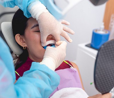 Gloved hands placing fluoride trays over girl’s teeth