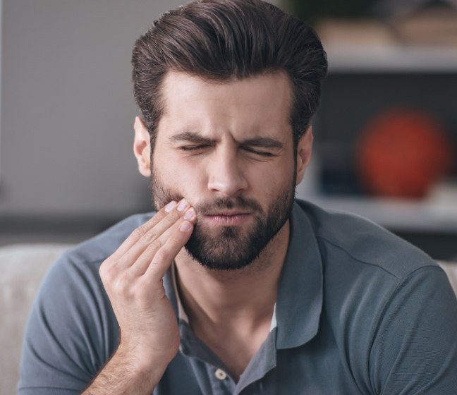 Man in need of emergency dentistry holding cheek in pain