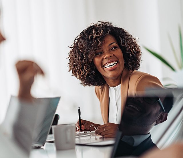 Woman at meeting smiling while holding a pen