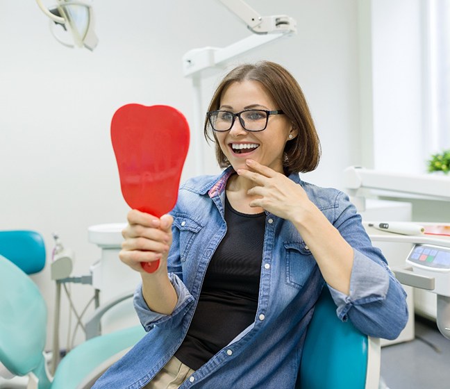 Woman in dental chair smiling while looking in mirror