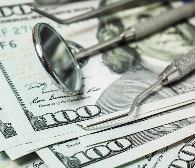 Dental tools laying on top of several hundred-dollar bills