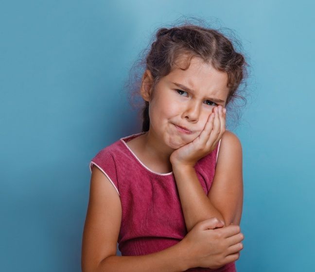 Young girl in need of emergency dentistry holding cheek