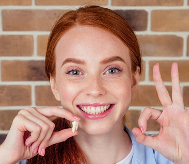 Woman holding removed tooth and smiling