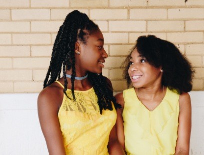 Mother and daughter smiling at each other in front of brick wall