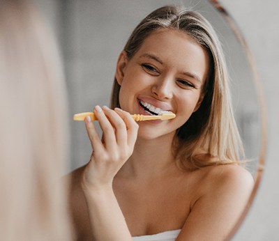 Woman smiling while brushing her teeth in bathroom