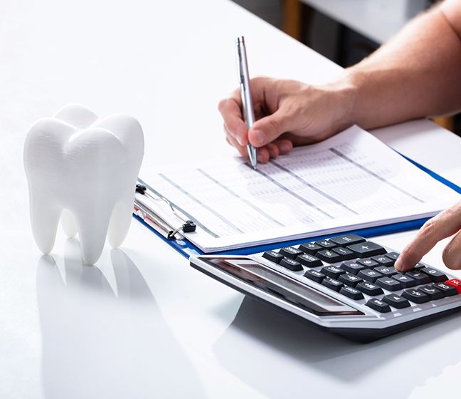 Patient calculating cost of treatment on desk next to model of tooth